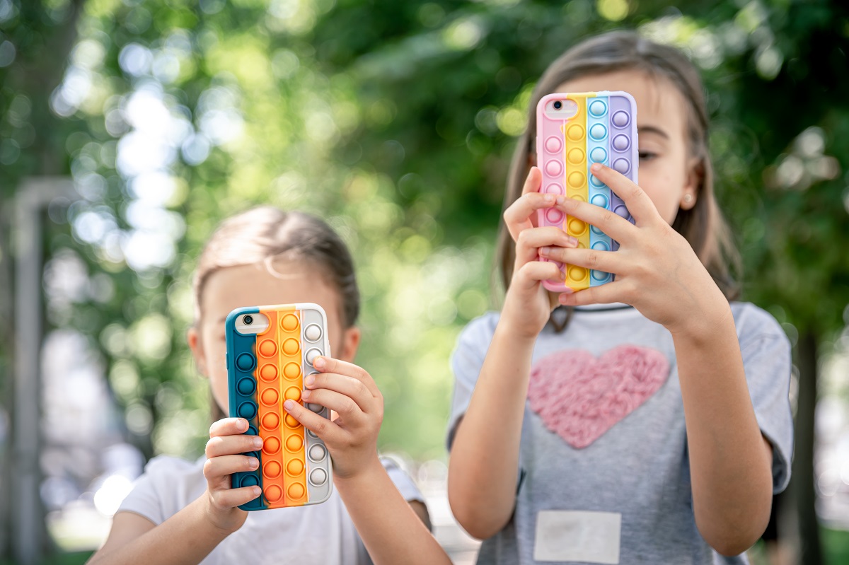 Little girls with phones in a case with pimples pop it, a trendy anti stress toy.